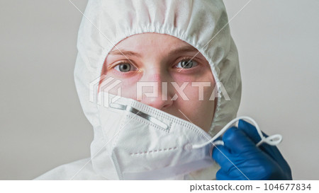 Infectious disease. Biohazard water. Contamination risk. Female lab specialist woman in gloves taking off face mask isolated on grey background. Infectious disease. Biohazard water. Contamination risk. Female lab specialist woman in gloves taking off face mask isolated on grey background. 104677834