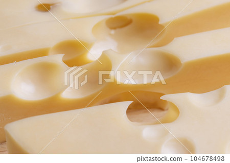 A cut piece of ripe cheese with lots of holes 104678498