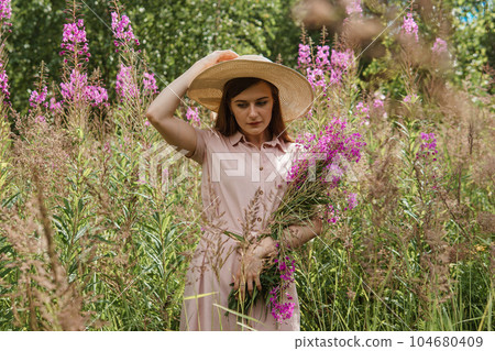 young woman in nature with a bouquet of pink wild flowers. A bouquet of Ivan-tea in the hands of a woman. 104680409
