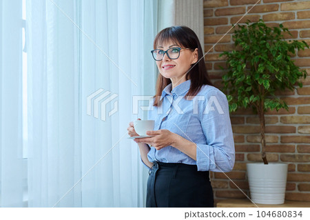 Middle-aged business woman with cup of coffee near window 104680834