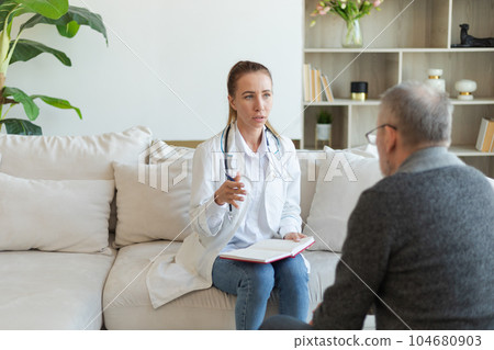 Female doctor examining older senior man in doctor office or at home. Old man patient and doctor have consultation in hospital room. Medicine healthcare medical checkup. Visit to doctor 104680903