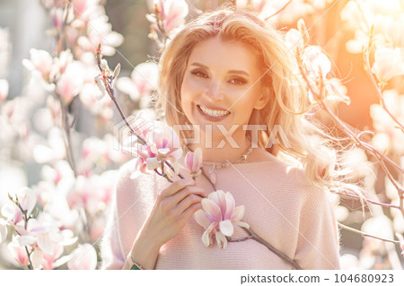 Magnolia woman portrait. Happy middle aged woman enjoying the smell in a blooming spring garden. Beautiful magnolia bushes, large flowers. 104680923