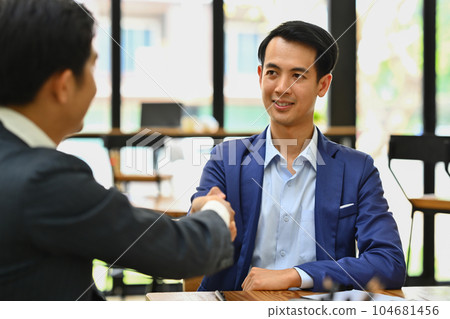 Confident businessman shaking hands closing deal with business partner or after successful negotiations at meeting Confident businessman shaking hands closing deal with business partner or after successful negotiations at meeting 104681456