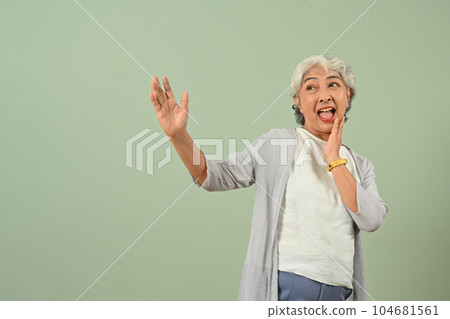 Excited gray haired senior woman posing over green pastel background 104681561