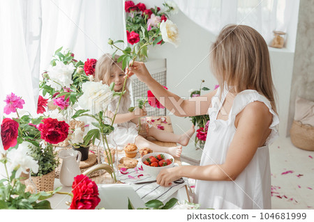 A little blonde girl with her mom on a kitchen countertop decorated with peonies. The concept of the relationship between mother and daughter. Spring atmosphere. A little blonde girl with her mom on a kitchen countertop decorated with peonies. The concept of the relationship between mother and daughter. Spring atmosphere. 104681999