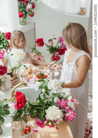 A little blonde girl with her mom on a kitchen countertop decorated with peonies. The concept of the relationship between mother and daughter. Spring atmosphere. A little blonde girl with her mom on a kitchen countertop decorated with peonies. The concept of the relationship between mother and daughter. Spring atmosphere. 104682000