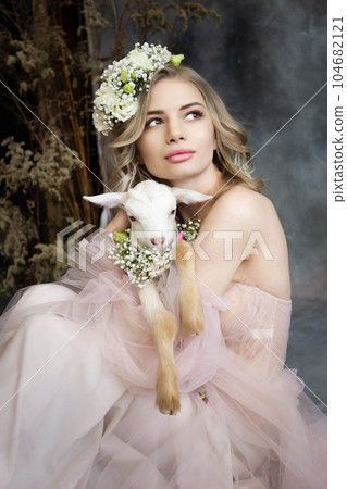 A young blonde woman in an airy pink dress with a white kid. Spring portrait of a woman. A young blonde woman in an airy pink dress with a white kid. Spring portrait of a woman. 104682121