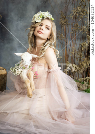 A young blonde woman in an airy pink dress with a white kid. Spring portrait of a woman. A young blonde woman in an airy pink dress with a white kid. Spring portrait of a woman. 104682134