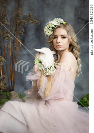 A young blonde woman in an airy pink dress with a white kid. Spring portrait of a woman. 104682136