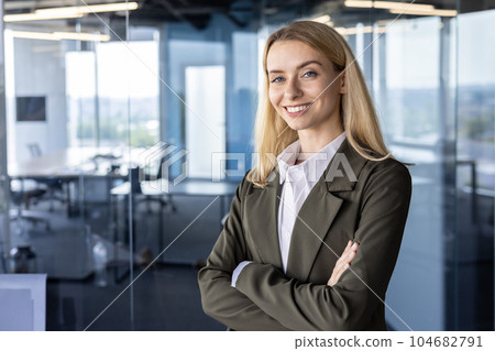 Portrait of a successful and smiling business woman, the founder of the company, the director in a suit standing confidently in the office. crossing his arms on his chest, looking at the camera. 104682791
