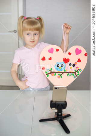 A blogger girl makes a felt craft for Valentine's Day in the shape of a heart. The concept of children's creativity and handmade. A blogger girl makes a felt craft for Valentine's Day in the shape of a heart. The concept of children's creativity and handmade. 104682908