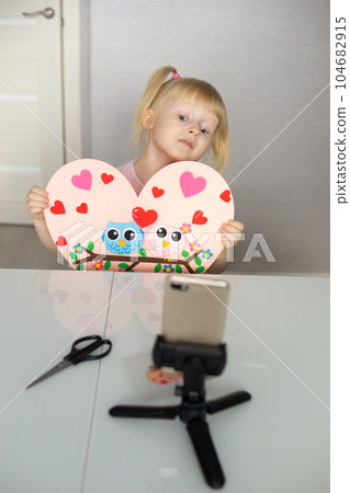 A blogger girl makes a felt craft for Valentine's Day in the shape of a heart. The concept of children's creativity and handmade. A blogger girl makes a felt craft for Valentine's Day in the shape of a heart. The concept of children's creativity and handmade. 104682915