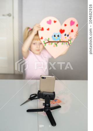 A blogger girl makes a felt craft for Valentine's Day in the shape of a heart. The concept of children's creativity and handmade. A blogger girl makes a felt craft for Valentine's Day in the shape of a heart. The concept of children's creativity and handmade. 104682916