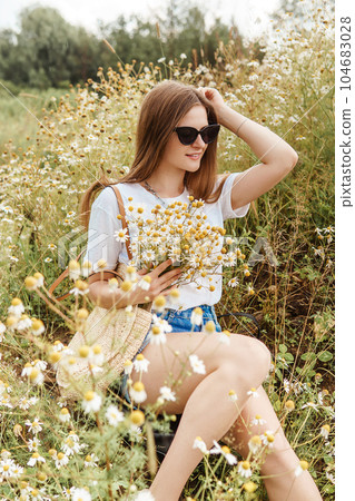 Beautiful young woman in nature with a bouquet of daisies. Field daisies, field of flowers. 104683028