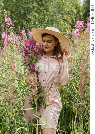 young woman in nature with a bouquet of pink wild flowers. A bouquet of Ivan-tea in the hands of a woman. 104683031