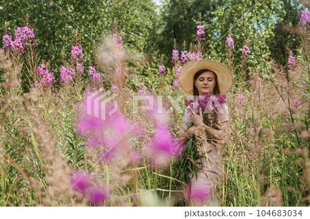 young woman in nature with a bouquet of pink wild flowers. A bouquet of Ivan-tea in the hands of a woman. 104683034