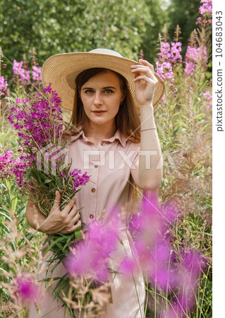 young woman in nature with a bouquet of pink wild flowers. A bouquet of Ivan-tea in the hands of a woman. 104683043