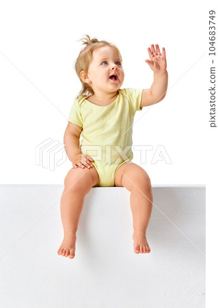 Curious, smart, delightful little girl, child, toddler in yellow clothes sitting and looking against white studio background Curious, smart, delightful little girl, child, toddler in yellow clothes sitting and looking against white studio background 104683749