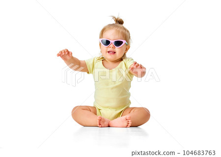 Cheerful, happy, little girl, toddler in yellow costume and sunglasses sitting on floor and smiling against white studio background Cheerful, happy, little girl, toddler in yellow costume and sunglasses sitting on floor and smiling against white studio background 104683763