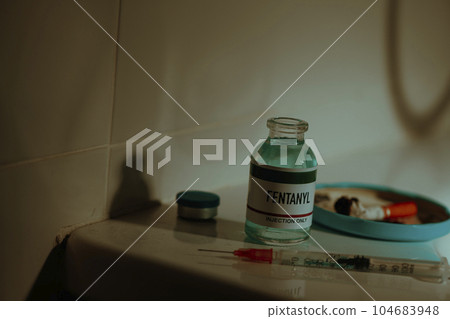 vial of fentanyl and syringe on a sordid toilet 104683948