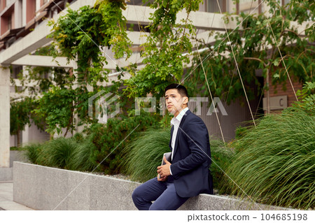 Businessman in formal wear sitting with laptop outside office. Urban, city, street background. 104685198