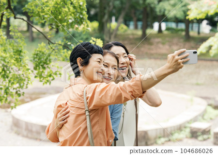 Middle-aged woman taking a picture with a smartphone with her friend Middle-aged woman taking a picture with a smartphone with her friend 104686026