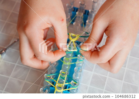 Hands of a girl playing with a knitting machine that knits with rubber bands. Hands of a girl playing with a knitting machine that knits with rubber bands. 104686312