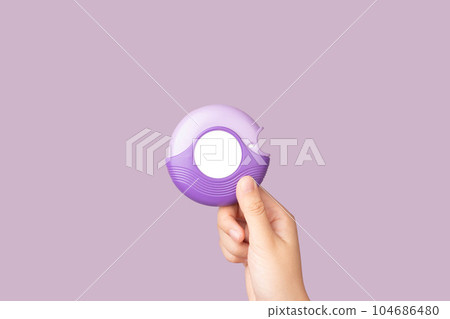 Asthma and COPD concept. Hand holding medicine dry powder inhaler on violet background. Pharmaceutical product is used to lung inflammation and prevent asthma attack. Asthma and COPD concept. Hand holding medicine dry powder inhaler on violet background. Pharmaceutical product is used to lung inflammation and prevent asthma attack. 104686480