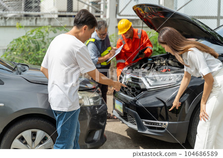 A Man and a woman pointing at the scratches on the car from the accident while car insurance agent and a machanic inspecting the car in the background 104686589