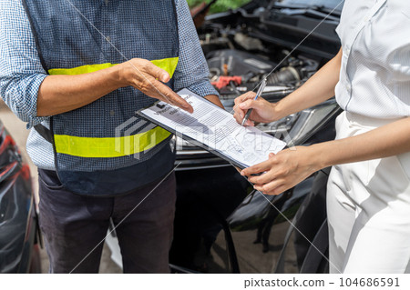 Close up of a car insurance agent showing the woman customer where to sign the car insurance claim form 104686591