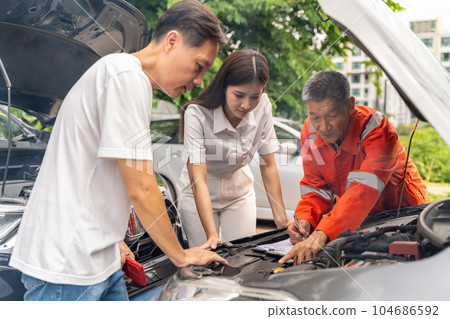 Car machanic showing the man and woman the problem of their car's engine while parking on the side of a road Car machanic showing the man and woman the problem of their car's engine while parking on the side of a road 104686592