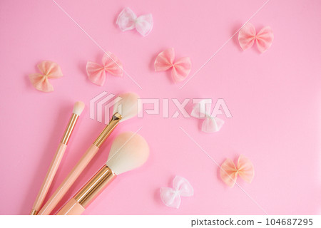 Three types of makeup brushes and a ribbon motif arranged on a pink background Three types of makeup brushes and a ribbon motif arranged on a pink background 104687295