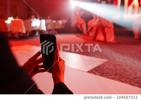 Women's hands with a smartphone take photos or videos of performances. 104687312