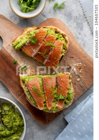 Toasts with salmon, guacamole avocado and herbs. Healthy food, top view Toasts with salmon, guacamole avocado and herbs. Healthy food, top view 104687505