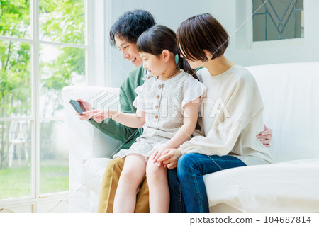 A family sitting on the sofa in the living room and looking at the smartphone 104687814