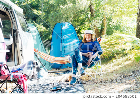 Adult woman relaxing, drinking tea while sitting in the travel chair near camper car vehicle and tents. Weekend trip activity. Female living on camper car and travel the world. Caravan car Vacation Adult woman relaxing, drinking tea while sitting in the travel chair near camper car vehicle and tents. Weekend trip activity. Female living on camper car and travel the world. Caravan car Vacation 104688501