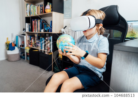 Boy studies space with help of technology and app. Kid in Virtual reality headset learning Solar system planets at home. Space explore with augmented reality glasses. Modern education science concept Boy studies space with help of technology and app. Kid in Virtual reality headset learning Solar system planets at home. Space explore with augmented reality glasses. Modern education science concept 104688513
