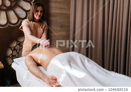 Rear view of unrecognizable man with shoulder pain having massage in medic clinic. Relaxation and revitalization of muscles after training. Female massage therapist making male athlete back massage. Rear view of unrecognizable man with shoulder pain having massage in medic clinic. Relaxation and revitalization of muscles after training. Female massage therapist making male athlete back massage. 104688516