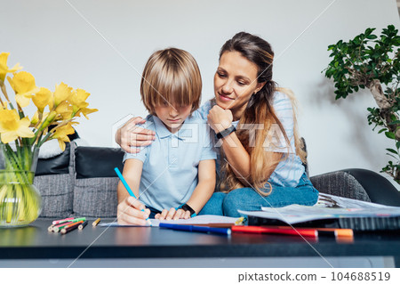 Mother and son drawing with color pencils and markers in the living room. Smiling mother has fun playing paint on paper with son on home family weekend, children creativity concept. Selective focus 104688519