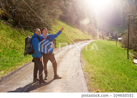 Two hikers are in the mountains in the spring nature outdoor. Hiking with backpacks. Two friends travel together in picturesque places. The man shows the way. Two men on a hiking trip in the mountains 104688581