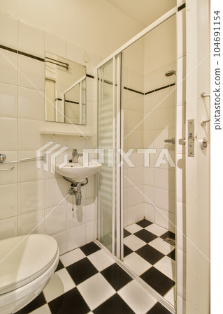 a white bathroom with black and white checkered tiles on the floor, shower stall door and toilet in the corner 104691154
