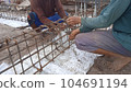 Worker's hands stringing iron rods with wire for beam section 104691194