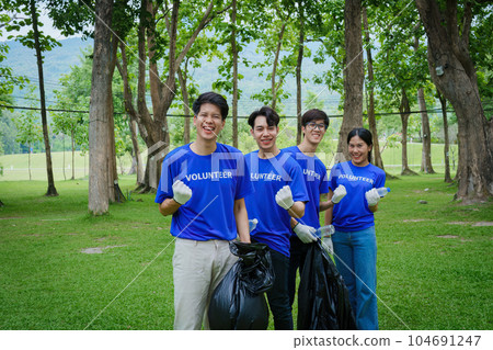 Volunteers of various nationalities are showing solidarity, donating their personal time, holding black trash bags to collect plastic waste for recycling to reduce pollution in a public park 104691247