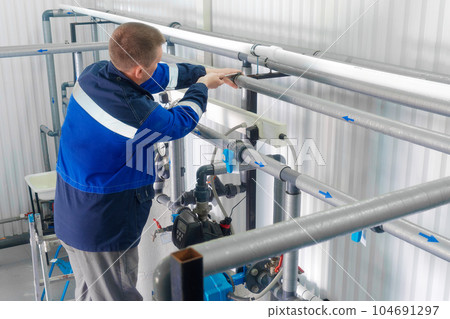 Professional locksmith checks pipes and water supply inside industrial building. Real worker 104691297