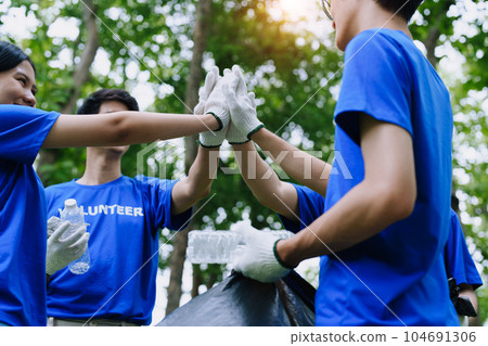 Volunteers of various nationalities are showing solidarity, donating their personal time, holding black trash bags to collect plastic waste for recycling to reduce pollution in a public park 104691306