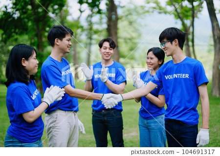 Volunteers of various nationalities are showing solidarity, donating their personal time, holding black trash bags to collect plastic waste for recycling to reduce pollution in a public park 104691317