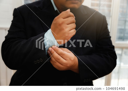 Businessman in black suit fastening buttons on the sleeves before the meeting. 104691498