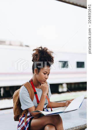 Asian teenage girl african american traveler dressed in casual wear holding map and searching right direction of route 104691641