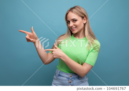 adorable girl in a casual outfit points to the empty space to the left on a blue background adorable girl in a casual outfit points to the empty space to the left on a blue background 104691767