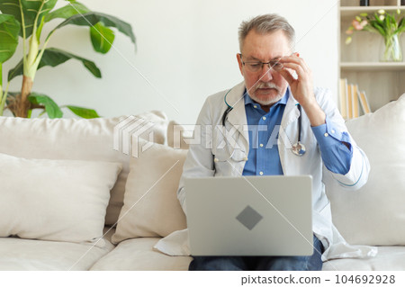 Senior man doctor working with laptop computer. Professional senior mature healthcare expert searching information or have online consultation in hospital room. Medicine healthcare medical checkup 104692928